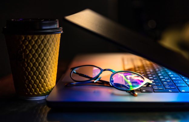 laptop half closed dark with colourful glow glasses paper cup